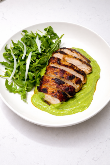 Sliced green‑seasoned chicken served with creamy avocado sauce and a fresh arugula salad.