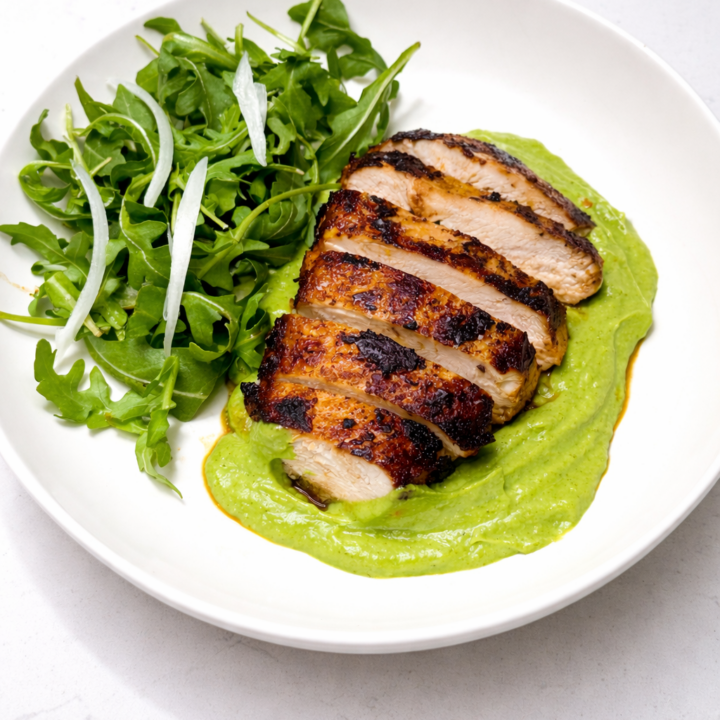 Sliced green‑seasoned chicken served with creamy avocado sauce and a fresh arugula salad.