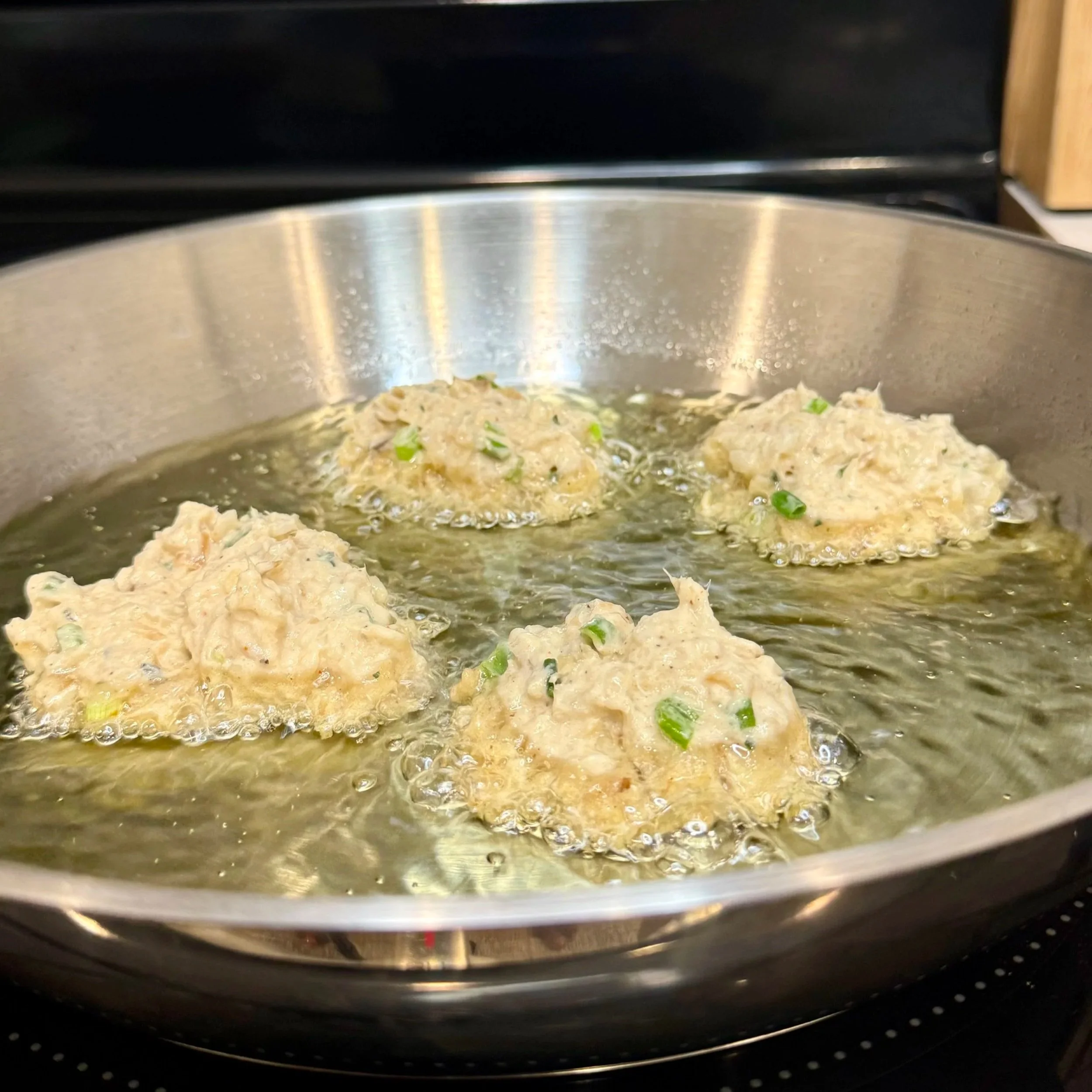 Batter dropped into hot oil, beginning the frying process for crispy Jamaican salt-fish fritters.