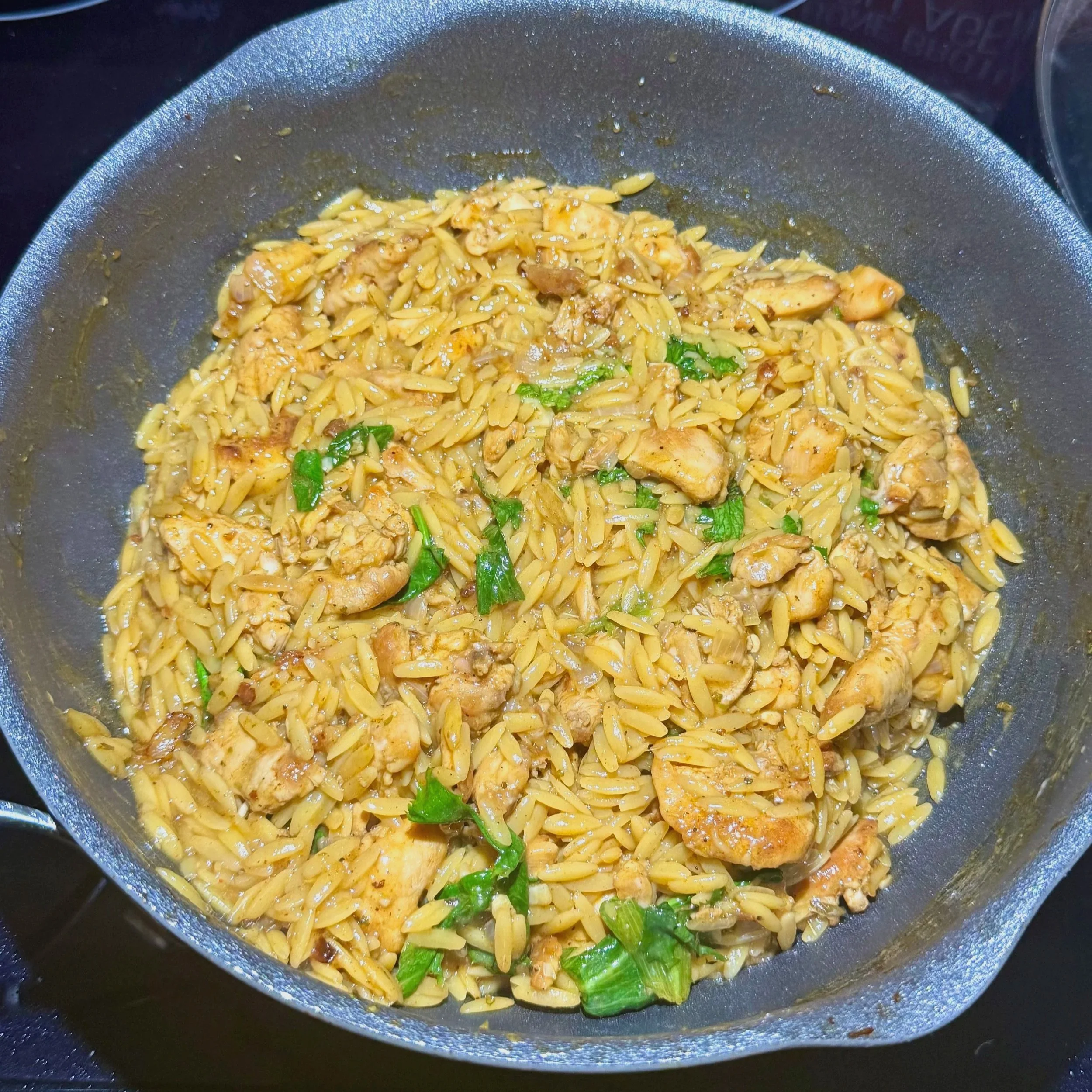   Finished chicken lemon orzo topped with Parmesan an herbs in a skillet  