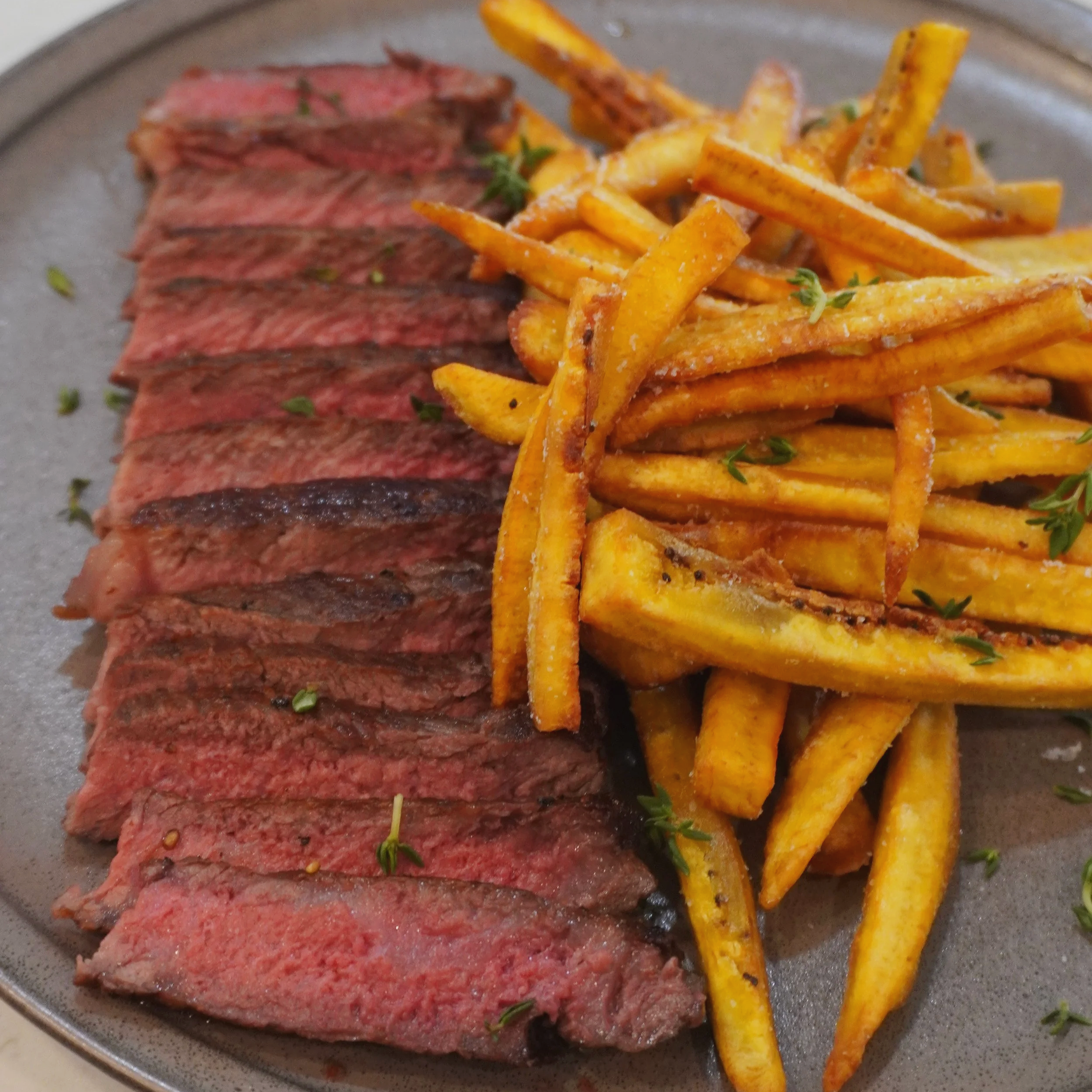 The finished Caribbean steak frites — seared Wagyu NY strip sliced and fanned on a plate, served alongside crispy golden plantain frites.