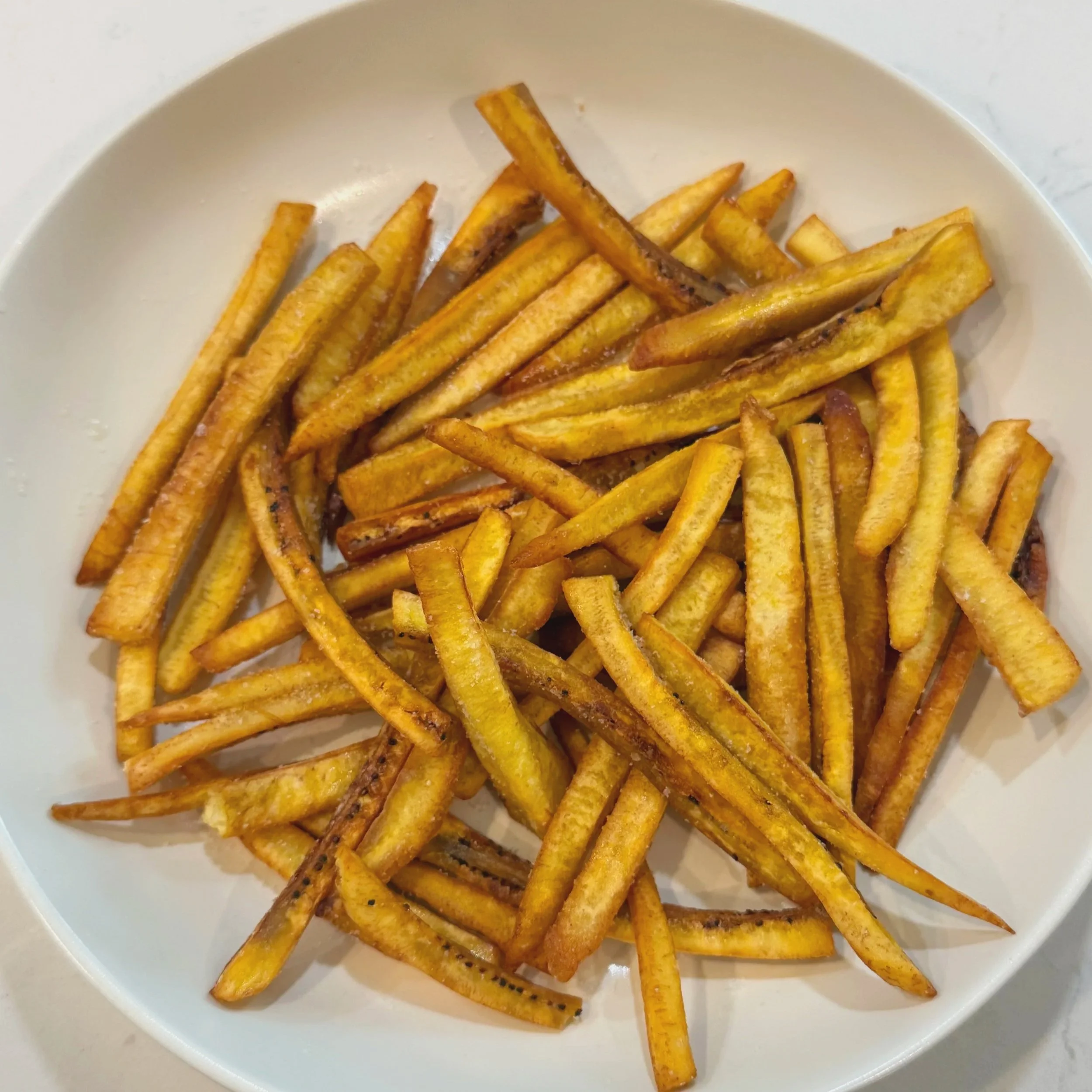 The finished double-fried plantain frites, deep golden and crispy, piled in a bowl and tossed with salt.