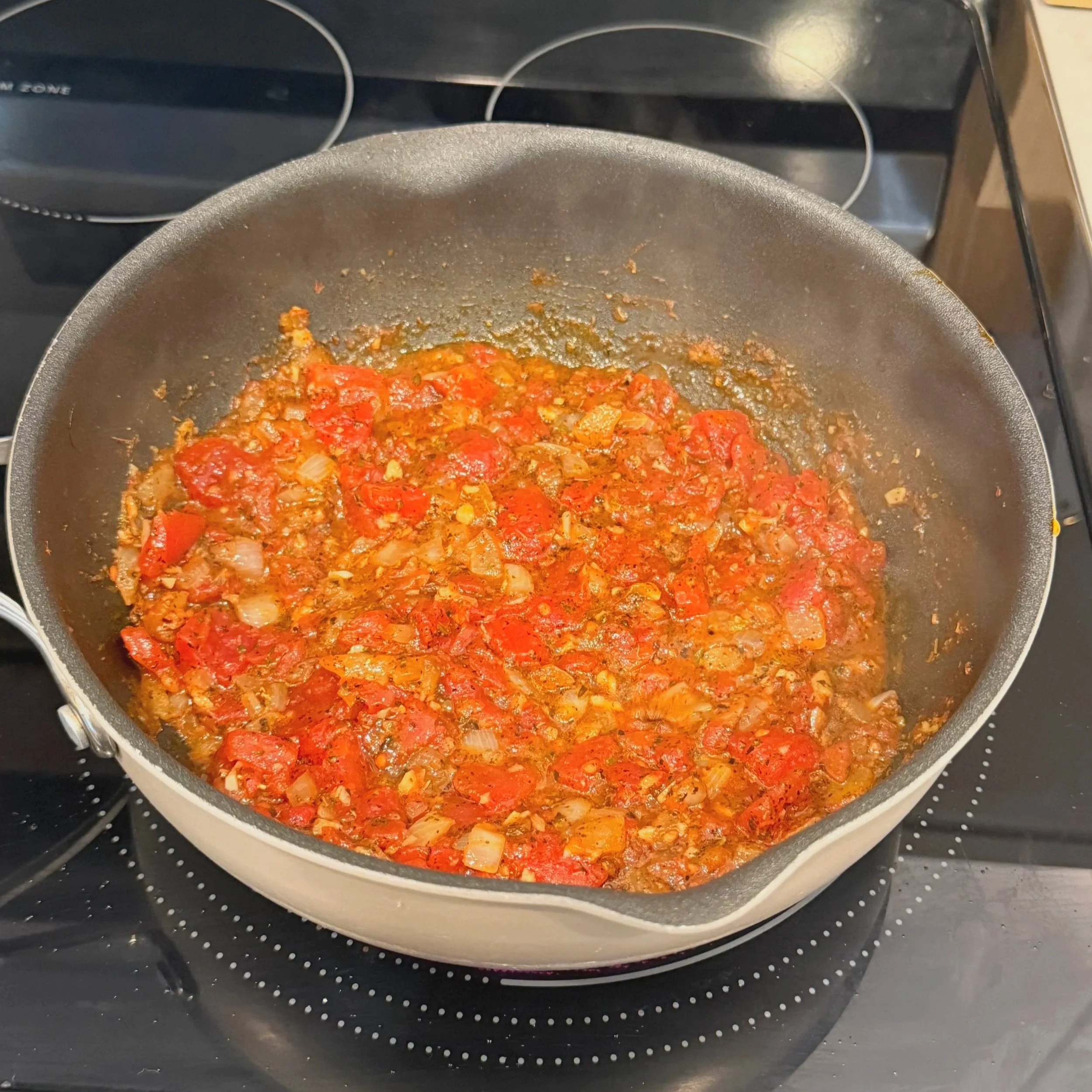 Diced tomatoes, oregano, basil, and red pepper flakes simmering into a sauce.