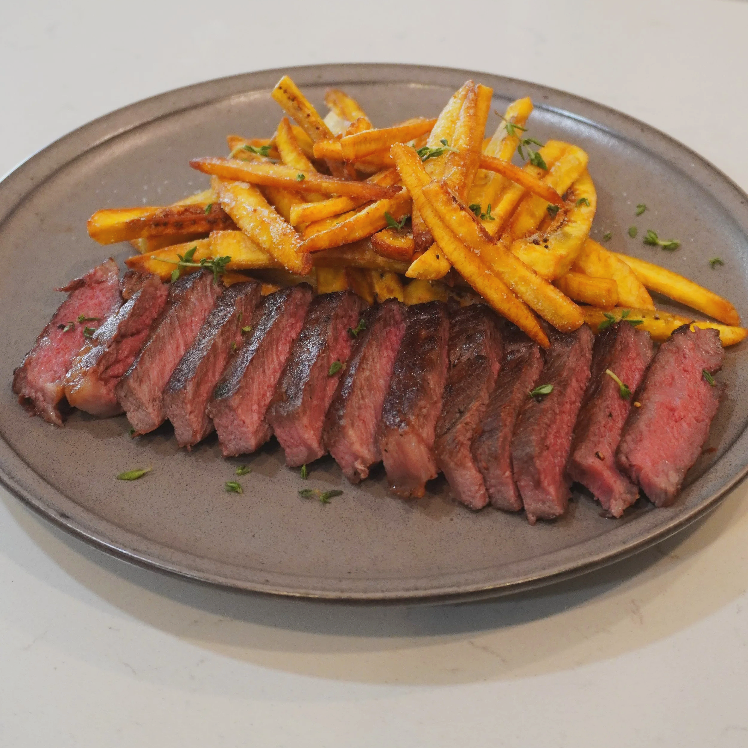 The completed Caribbean steak frites dish — sliced Wagyu steak with scotch bonnet-garlic butter, plated with a generous pile of crispy plantain frites, ready to serve.