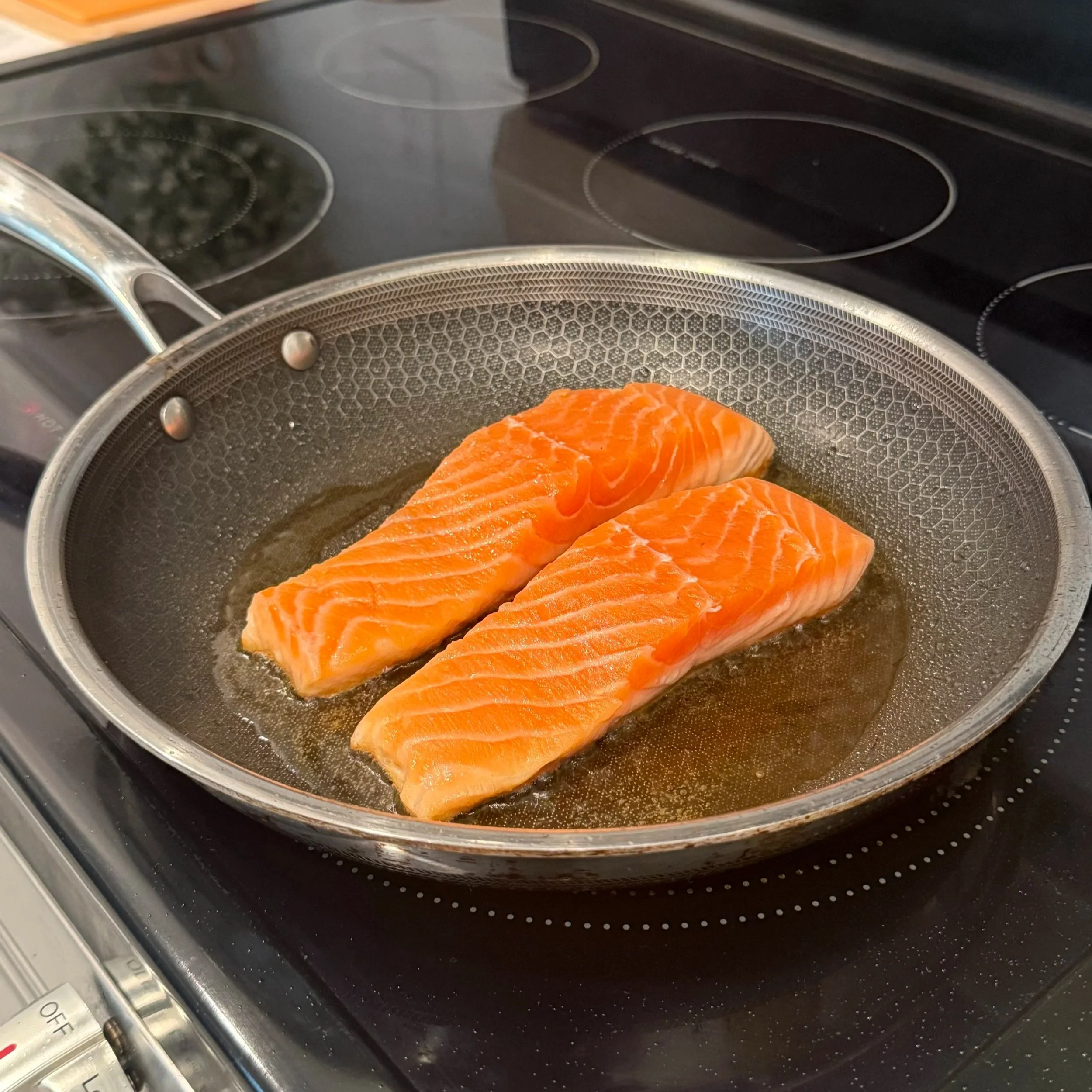  Salmon fillets searing skin-side down in a hot pan, the skin turning golden and crisp. 