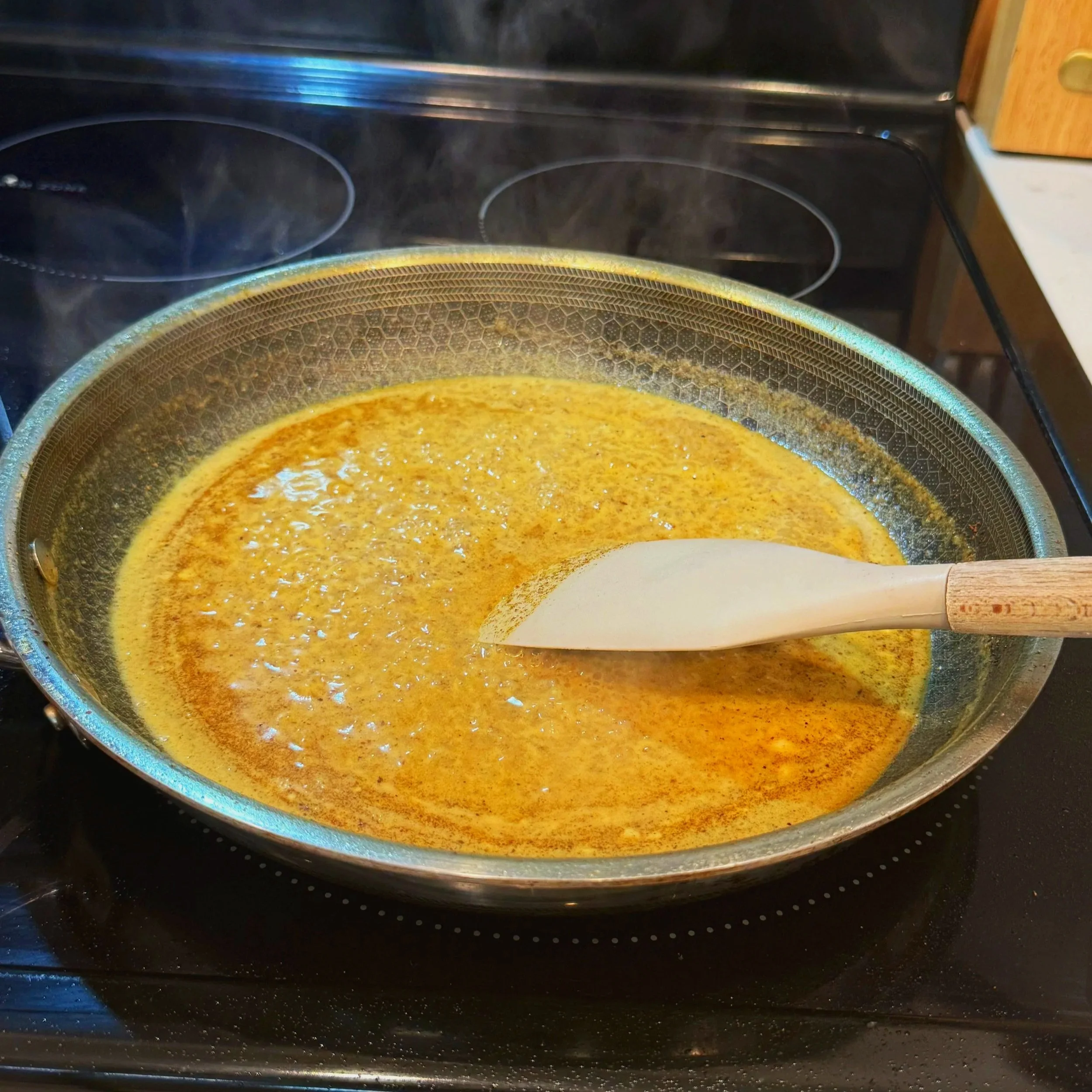  A creamy coconut curry sauce simmering in a pot, with visible ginger, spices, and a golden hue from the curry powder and paprika. 