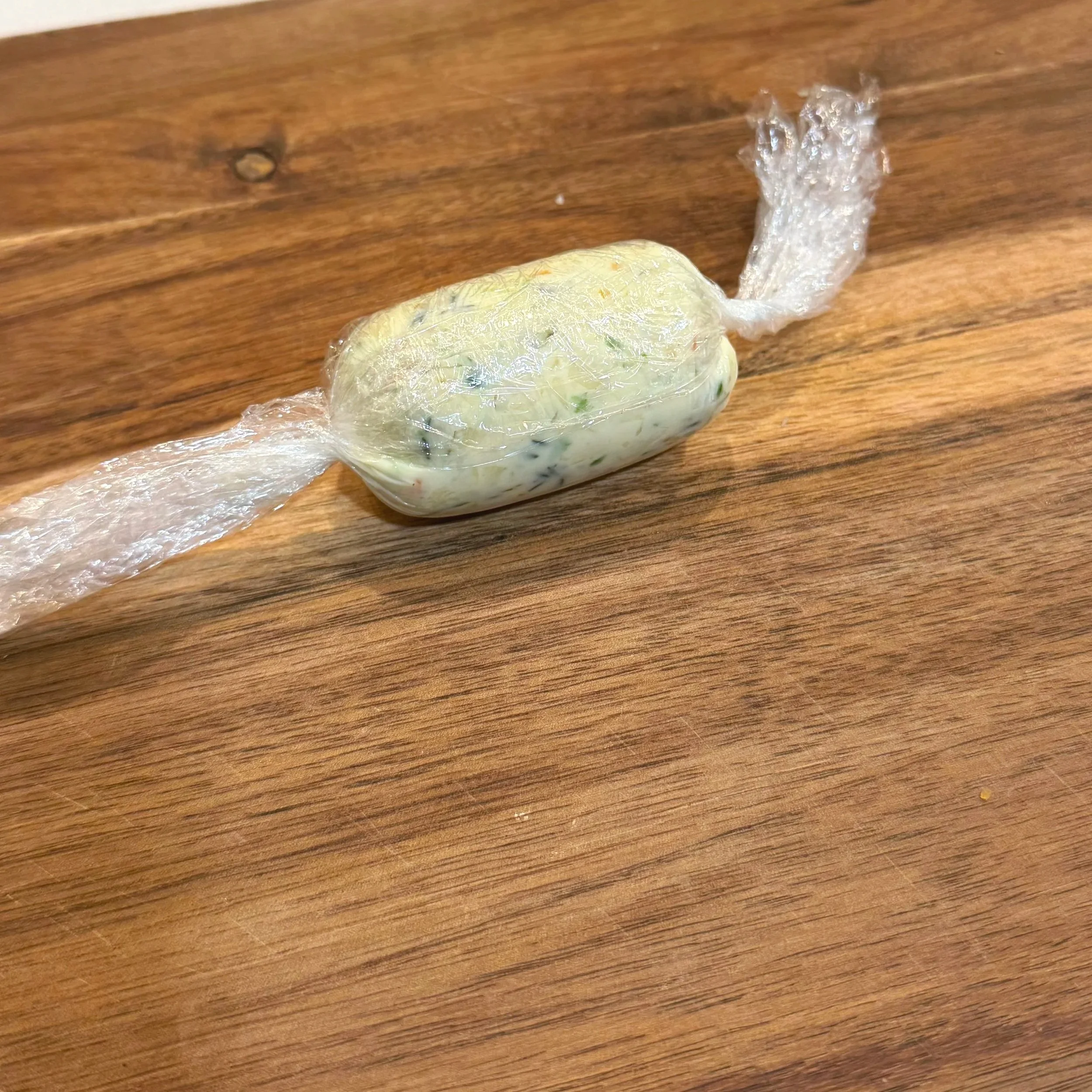 The scotch bonnet-garlic compound butter shaped into a log and wrapped in plastic, ready to chill before slicing into coins.
