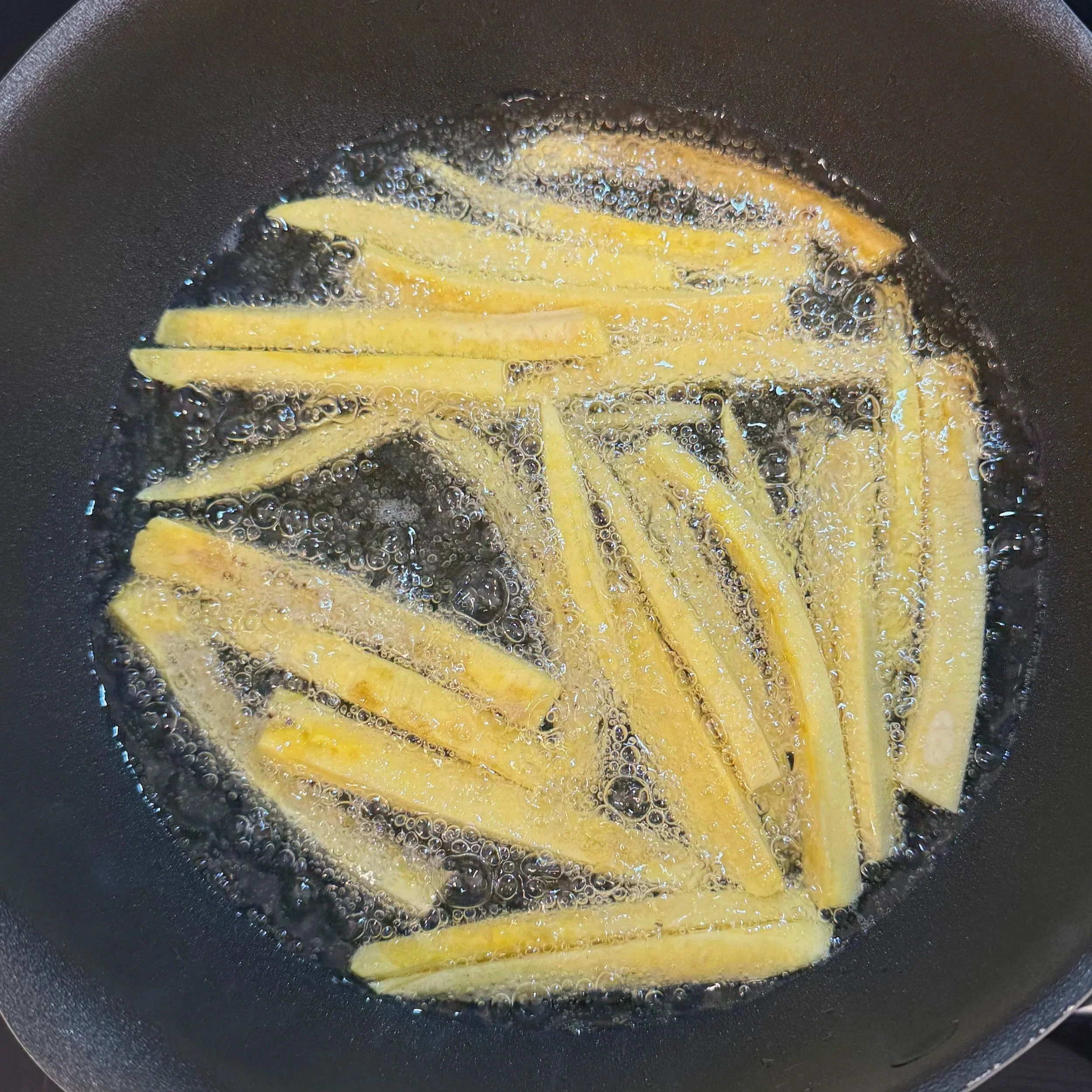 Plantain batons frying in hot oil, turning golden as they crisp up in the pan.