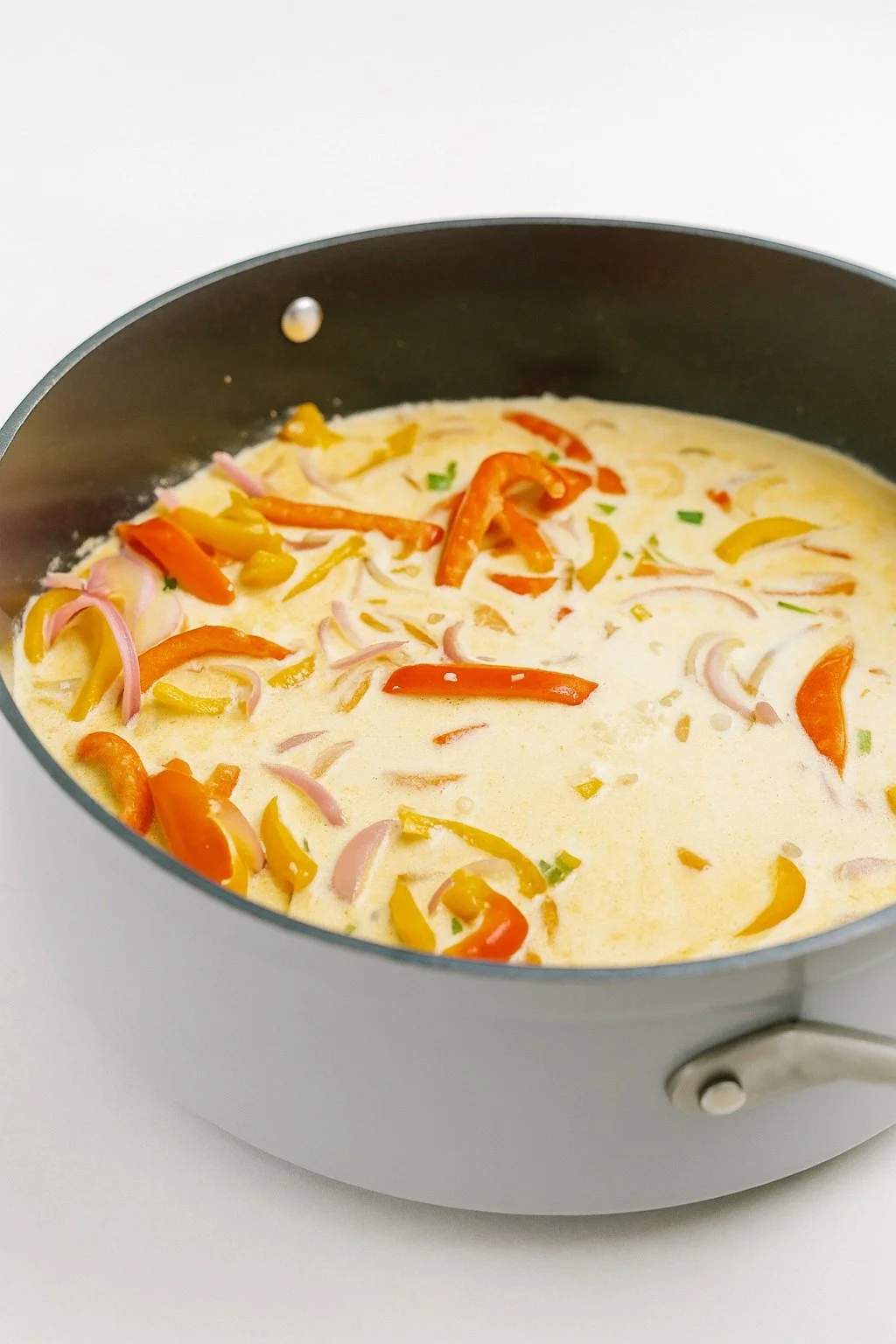  Skillet of creamy Rasta Pasta simmering with red and yellow bell peppers and sliced onions in a rich coconut-based sauce, perfect for pairing with jerk chicken. 